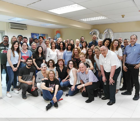 Gran grupo de personas posando juntas en una sala, con globos con el número 30 al fondo